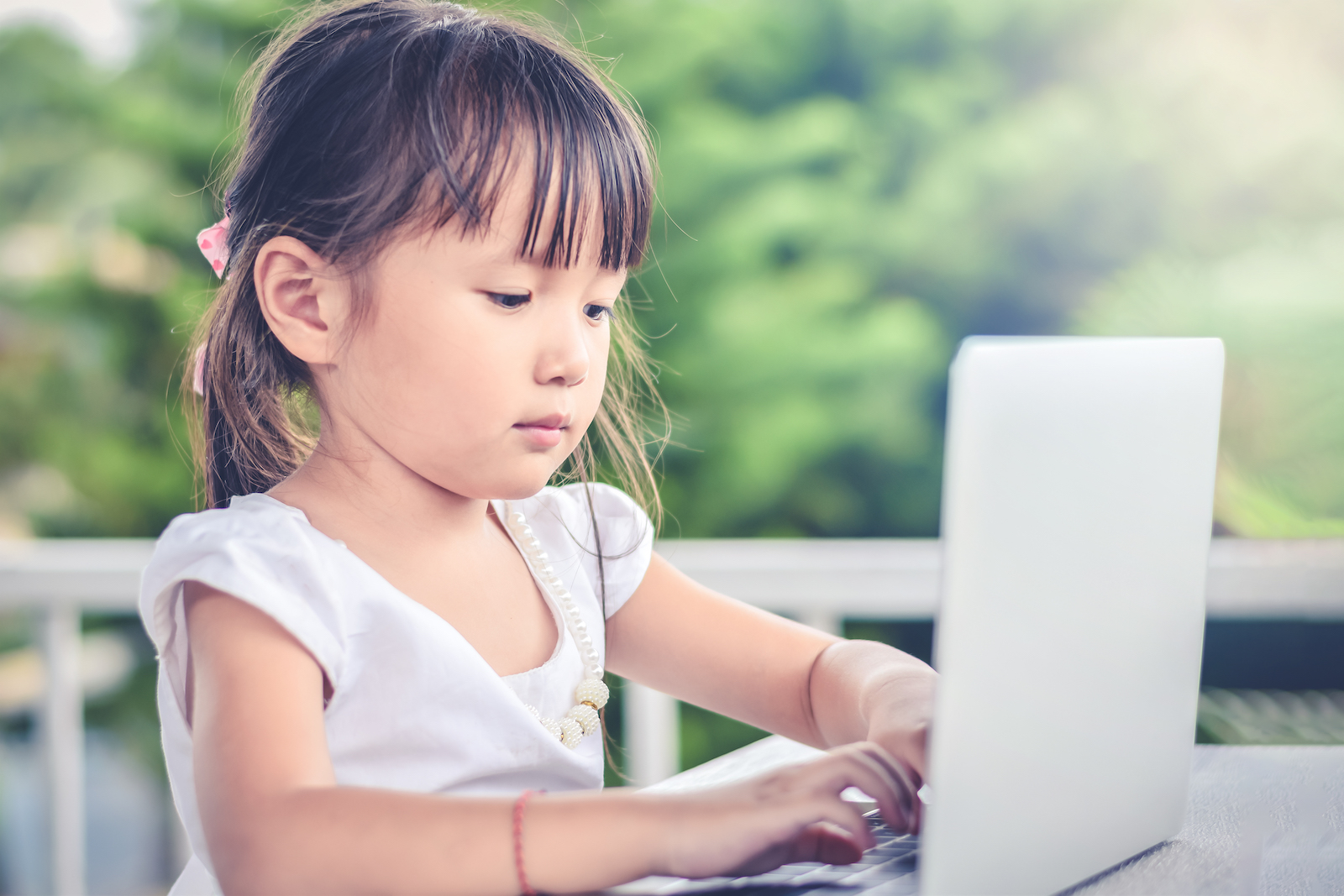 Asian little girl outdoors with smiley face using laptop in the garden at home. family activity concept.