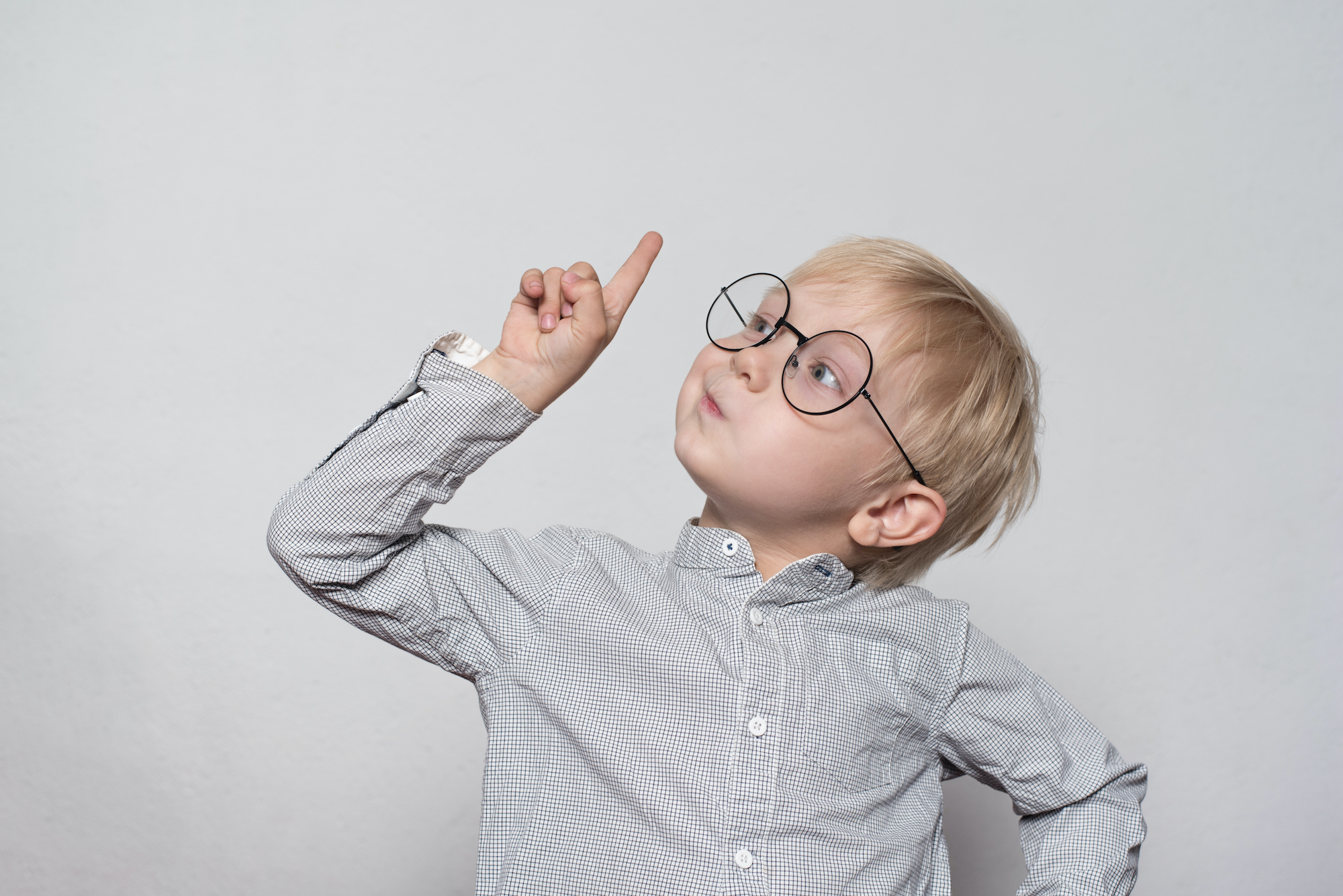 Portrait of a cute blond boy with big glasses. Finger pointing up. White background.